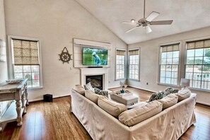 A living room with a sofa, television, fireplace, and large windows. - Bear Trap Dunes * 4BR Luxury townhouse (Ocean View)