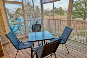 Un espace extérieur abrité, doté d’une table et de chaises, offrant une vue sur le paysage environnant et comprenant une terrasse en bois.