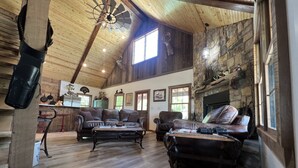A spacious living room with a high ceiling, wooden beams, a stone fireplace, leather furniture, and a large window. - LODGE AT SADDLE RIDGE. Just five minutes from Hermann. (Hermann)