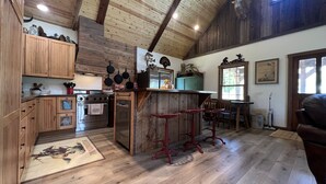 A rustic kitchen with wooden cabinets, a central island, and a dining area with red bar stools. - LODGE AT SADDLE RIDGE. Just five minutes from Hermann. (Hermann)
