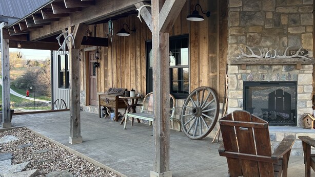 A rustic outdoor seating area with wooden furniture, a stone fireplace, and a stone wall. - LODGE AT SADDLE RIDGE. Just five minutes from Hermann. (Hermann)