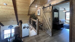 A rustic interior with wooden beams, a sliding barn door, a bed, and a ceiling fan. - LODGE AT SADDLE RIDGE. Just five minutes from Hermann. (Hermann)