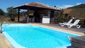 Ein Pool mit gefliestem Sonnendeck, Liegestühlen und einem überdachten Bereich mit einer gefliesten Dachfläche.