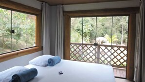 Ein Schlafzimmer mit Bett, Vorhängen und Blick auf eine Holzterrasse und Grünfläche.