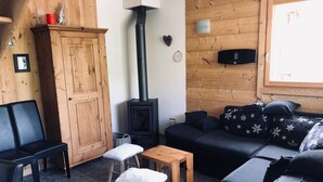 A cozy living room with a wooden interior, a black sofa, a wooden table, and a fireplace. - Chalet with nice view, garden and hot tub. Ideal for skiing and cycling! (Valloire)