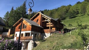 A wooden chalet with a balcony, set on a hillside with a clear blue sky. - Chalet with nice view, garden and hot tub. Ideal for skiing and cycling! (Valloire)