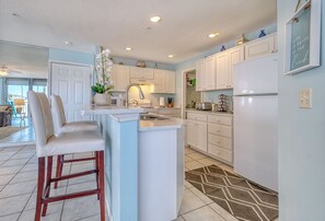 A modern kitchen with white cabinets, a central island with bar stools, a refrigerator, and a decorative wall sign.