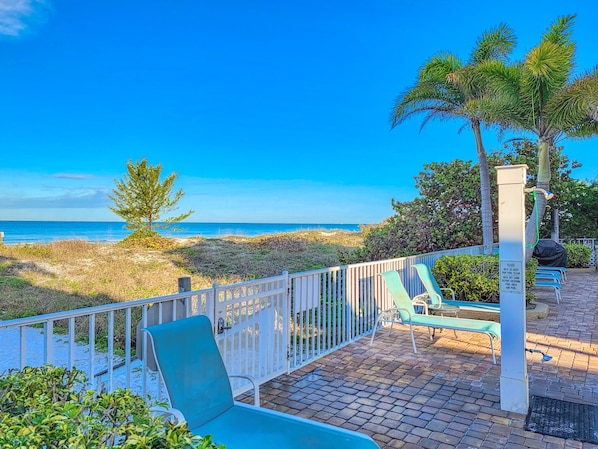 A patio with a view of the beach and ocean, a pool, and lounge chairs.