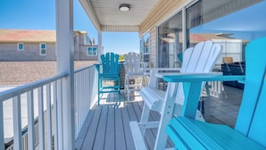 A wooden deck with white and turquoise Adirondack chairs, a table, and a glass railing overlooking a beach. - Newly Remodeled Coastal Beachside Vacation Rental!! (Indian Rocks Beach)