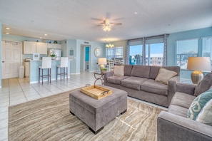 A spacious living room with a grey sofa, a wooden coffee table, and a dining area with white chairs.
