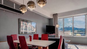 Une chambre d’hôtel moderne dotée d’un coin repas, d’un téléviseur à écran plat et d’une grande fenêtre donnant sur la ville.