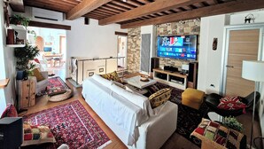 A spacious living area with a high ceiling, a television, and a stone wall.
