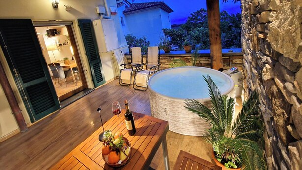 An outdoor patio with a hot tub, wooden furniture, and a stone wall.