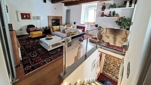 A spacious living area with a sofa set, a coffee table, and a patterned rug. A staircase with a glass railing leads to an upper level.