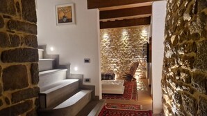 A staircase leading to a room with a stone wall and a red patterned rug.