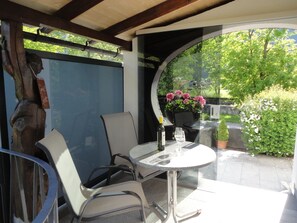 Une terrasse extérieure avec une table ronde, deux chaises, une bouteille de vin et un pot de fleurs orné de fleurs roses.