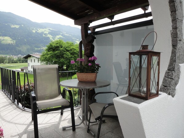 Un balcon avec une table, des chaises, un pot de fleurs et une lanterne.