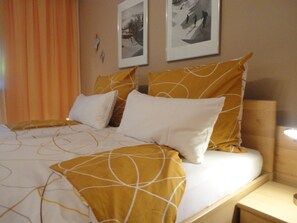 Un lit recouvert d’une couvre-lit à motifs blancs et jaunes, avec deux oreillers blancs et une tête de lit en bois.