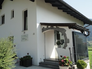 Um edifício com uma entrada em arco de pedra, uma placa indicando 'Apartment bei Anna', e plantas em vasos na parte externa.