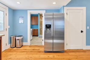 A kitchen with a stainless steel refrigerator, wooden cabinets, and a trash can. - Home Squared by LUX Retreats Paso (Paso Robles)