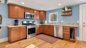 Una cocina con gabinetes de madera, electrodomésticos de acero inoxidable, encimera de mármol y lavavajillas empotrado.