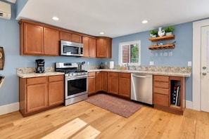 A kitchen with wooden cabinets, stainless steel appliances, a marble countertop, and a built-in dishwasher. - Home Squared by LUX Retreats Paso (Paso Robles)
