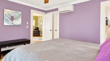 Quarto com cama, ventilador de teto, ar condicionado e porta que dá para outro cômodo.