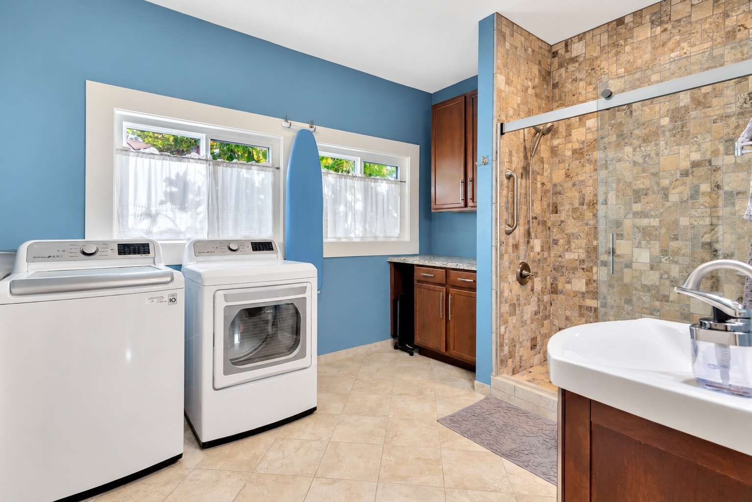 A laundry area with two washing machines, a shower with a tiled wall, and a sink with a countertop.