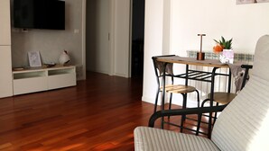 Una sala de estar con suelo de madera, un televisor de pantalla plana en la pared, una mesa de comedor con sillas y un sofá.