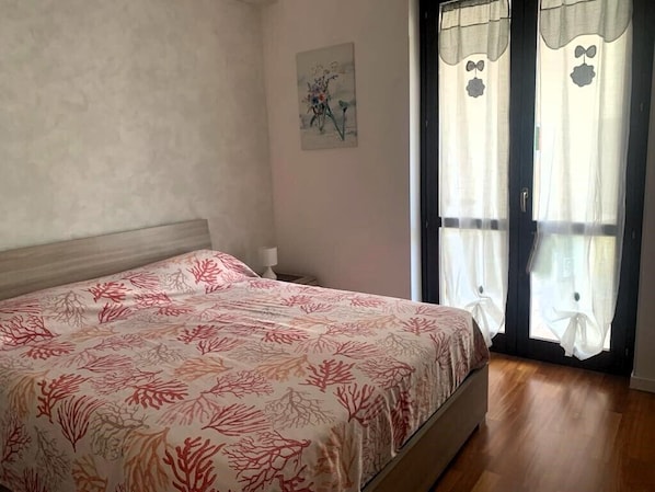 A bedroom with a bed, a door with curtains, and a wall with a painting. - Butterfly cottage (Puglia)
