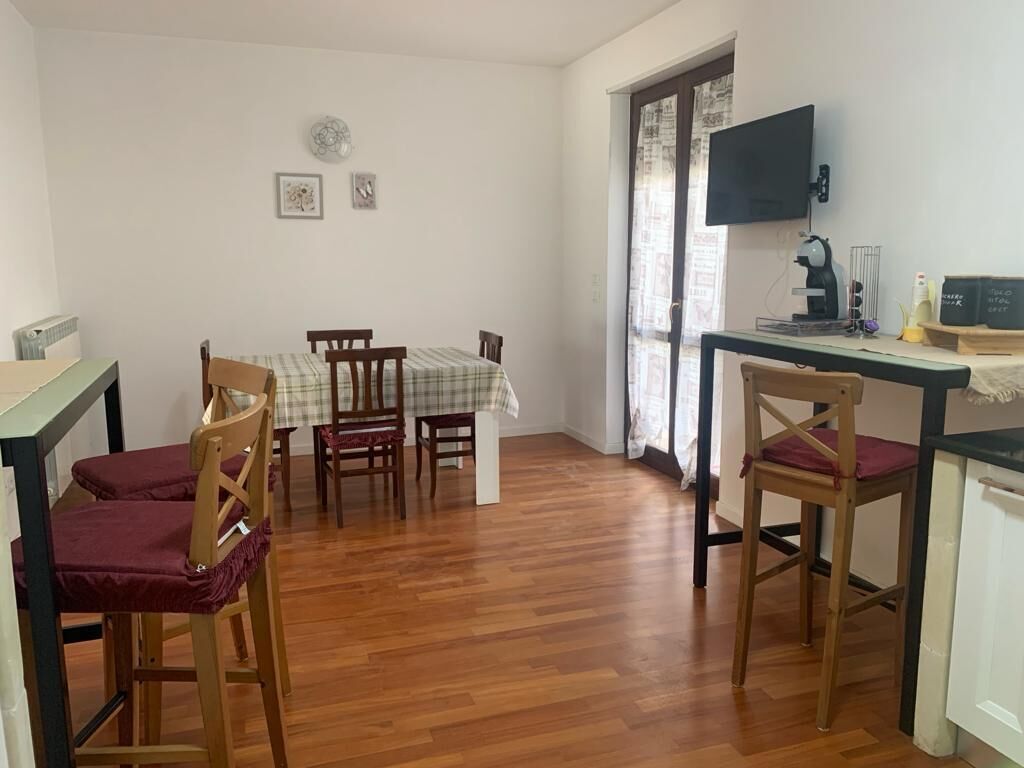 Un comedor con una mesa y sillas, un televisor en la pared, y una ventana con cortinas.