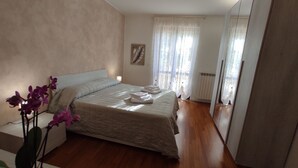 Un dormitorio con cama, mesita de noche, radiador y ventana con cortinas.