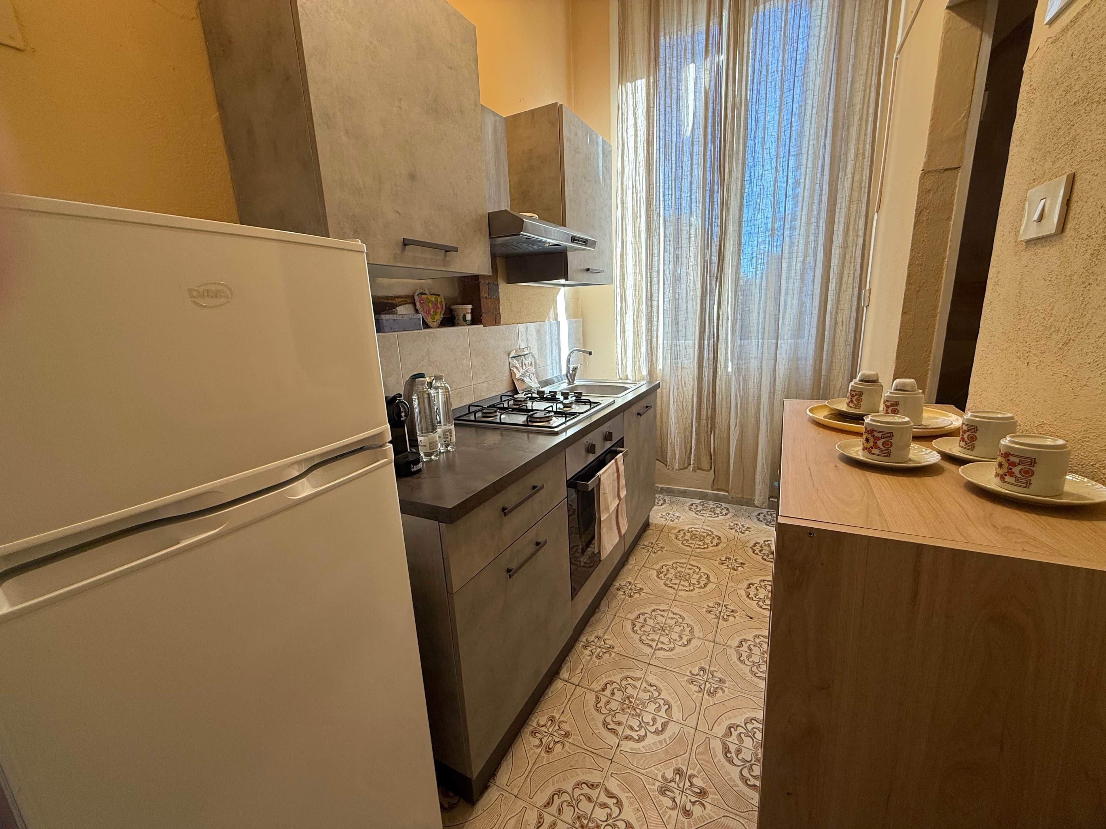 A compact kitchen with a refrigerator, stove, and sink. There are decorative items on the counter and a tray with cups on the right side.