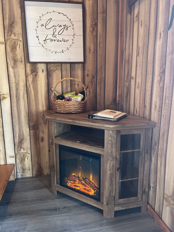 Un rincón acogedor con chimenea, una cesta de mimbre con objetos y un cartel enmarcado.