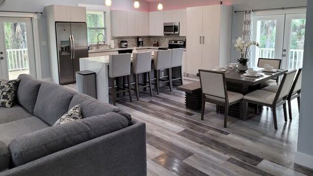 A modern kitchen with a central island, bar stools, and a dining table with chairs. - Pine Ridge Model Home (Naples)
