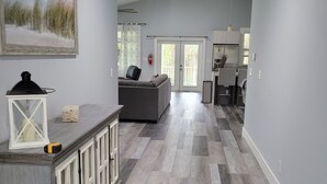 A spacious living area with a gray sofa, a dining table, and a kitchen in the background. - Pine Ridge Model Home (Naples)