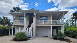 A two-story house with a covered front porch, a garage, and a staircase leading to the upper level. - Pine Ridge Model Home (Naples)