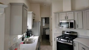 A narrow kitchen with white cabinets, a stainless steel refrigerator, a microwave, and a stove. - 038 Tiny Home nr Grand Canyon South Rim Sleeps 4 (Williams)