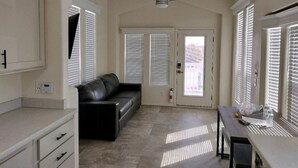 A spacious living area with a black leather sofa, a dining table, and a ceiling fan. - 038 Tiny Home nr Grand Canyon South Rim Sleeps 4 (Williams)