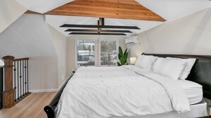 Un dormitorio con techo inclinado, una cama grande, una mesita de noche, una planta en maceta y vistas a través de un ventanal.