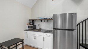 Una cocina moderna con armarios blancos, un refrigerador de acero inoxidable, un microondas y una cafetera sobre la encimera.
