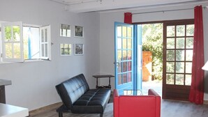 Ein Raum mit einer schwarzen Ledersofa, einem roten Sessel, einem kleinen Tisch und einer blauen Tür, die nach draußen führt.