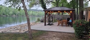 A gazebo with a swing chair, outdoor seating, and a view of a lake.