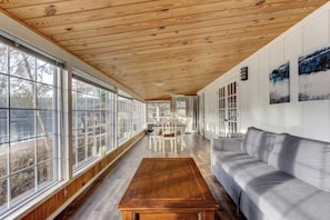 Una habitación amplia con ventanas grandes, techo de madera y sofá gris.