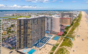 A high-rise hotel with multiple floors, a swimming pool, and a beach view.