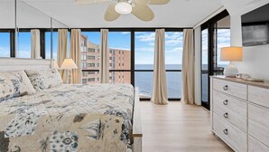 Une chambre à coucher avec un lit, un ventilateur de plafond, une commode et une vue sur l’océan.
