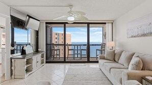 Un salon spacieux avec balcon, ventilateur de plafond, télévision et vue sur la mer.