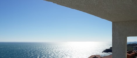 A coastal view from a balcony with a clear sky, ocean, and distant land.