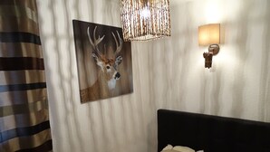 A bedroom with a bed, pillows, a wall-mounted lamp, a painting of a deer, and a striped curtain. - Duplex 6-8 people Saint François Longchamp (Saint-François-Longchamp)