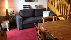 A living room with a dark grey sofa, a wooden dining table, and a staircase with wooden railings. - Duplex 6-8 people Saint François Longchamp (Saint-François-Longchamp)
